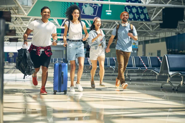 Mutlu gülümseyen turist grubu uçağa yetişmek için kapıya doğru koşuyor.