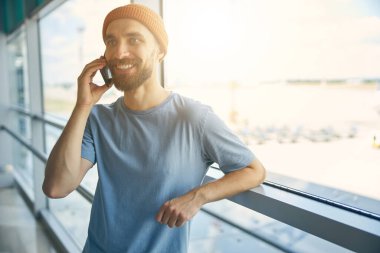 Cam pencerenin önünde duran turuncu şapkalı mutlu adam.