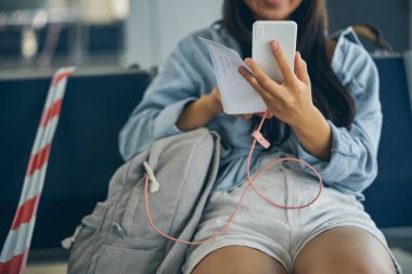 Biletli ve modern aletli güzel bir kadın bankta oturuyor.