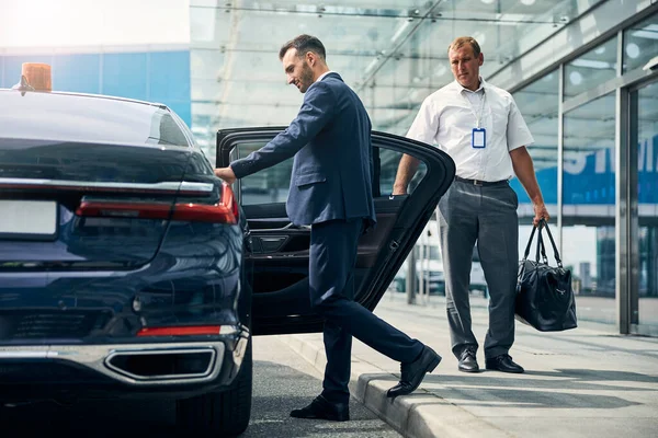 Homem em um belo terno abrindo um carro para começar a viajar do aeroporto — Fotografia de Stock