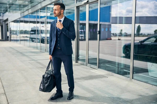 Yorgun görünüşlü bir adam çantasıyla havaalanından çıkıyor.