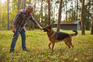 Mutlu yaşlı vatandaş dışarıda köpeğiyle oynuyor.