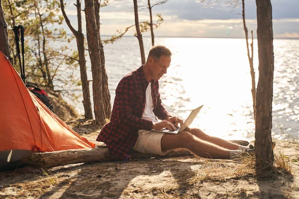 Uomo allegro utilizzando il computer portatile durante il campeggio in natura — Foto Stock