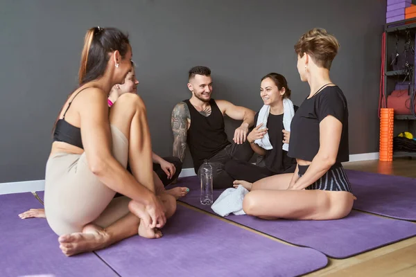 Sporty group of fitness class sitting on purple mats and talking together — Stock Photo, Image