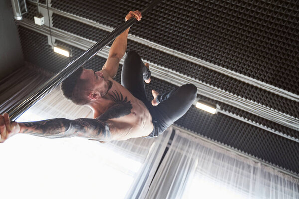 Handsome man performing pole dance moving on pole