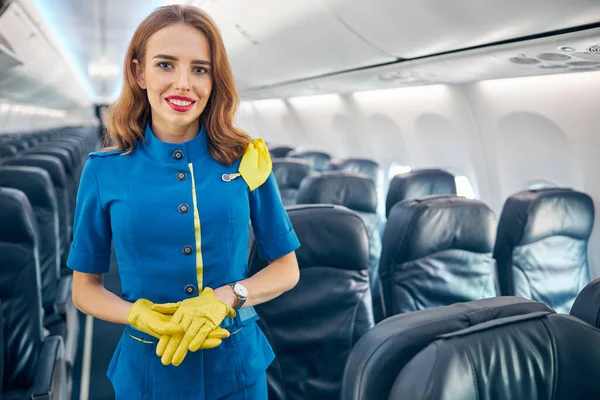 Kobieta stewardessa trzyma ręce skrzyżowane patrząc na aparat fotograficzny na pokładzie samolotu komercyjnego — Zdjęcie stockowe