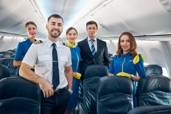 Happy friendly aviation staff posing and looking at the photo camera in salon of aircraft — Stock Photo, Image