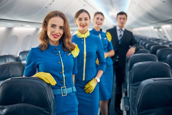 Χαρούμενη χαρούμενη αεροπορική ομάδα σε κομψό μπλε και σκούρο μπλε στολή στέκεται στο σαλόνι του αεροπλάνου — Φωτογραφία Αρχείου