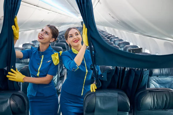 Beautiful females air hostesses in blue uniform with yellow scarf and gloves preparing plane to the passenger — Stock Photo, Image