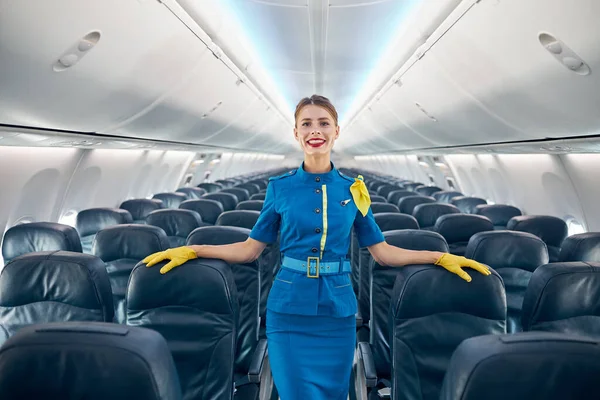 Beautiful air hostess posing at the photo camera in aisle of empty commercial airplane