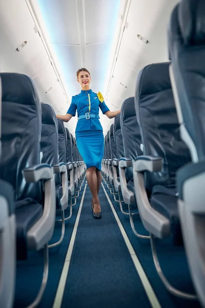 Happy smiling air hostess wearing suit standing near the cozy passenger chairs — Stock Photo, Image