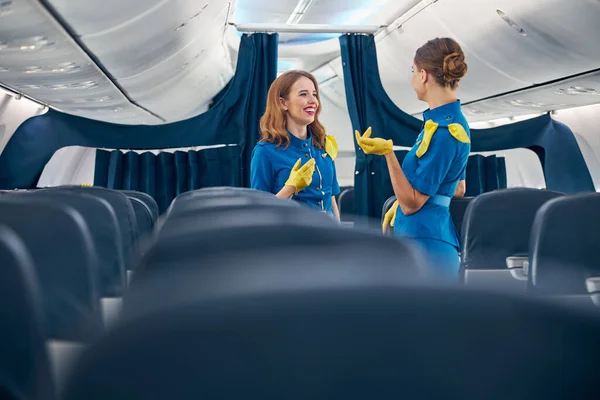 Felices damas bonitas usando traje de azafata hablando juntas en la primera clase de avión — Foto de Stock