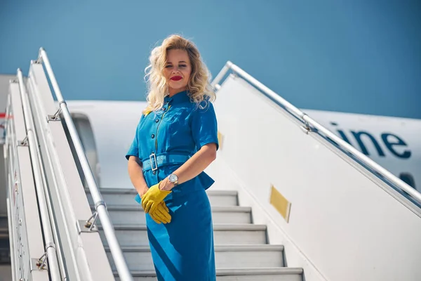 Azafata encantadora de pie en las escaleras del avión bajo el cielo azul —  Fotos de Stock