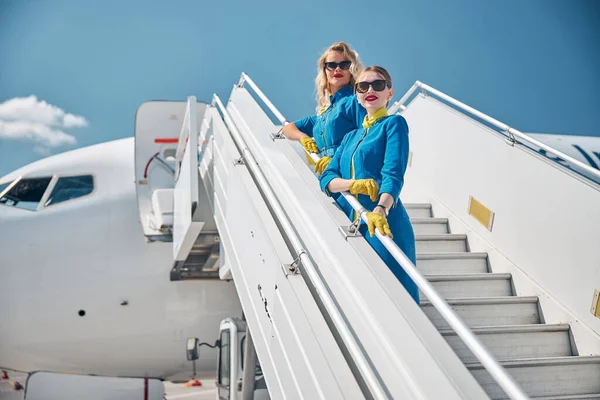 Krásné letušky stojící na schodech letadla pod modrou oblohou — Stock fotografie