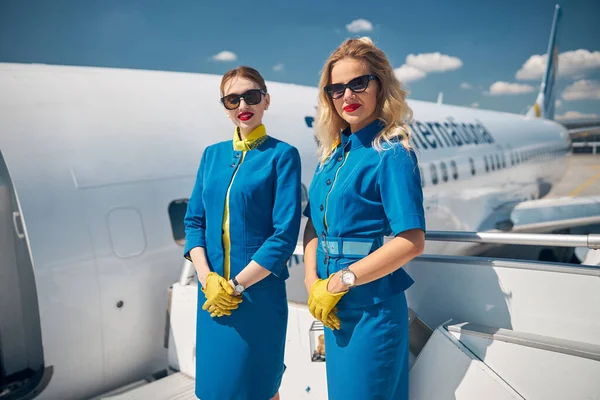 Hermosas azafatas jóvenes de pie en las escaleras del avión — Foto de Stock