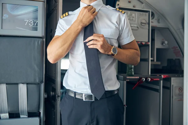 Młody kapitan dopasowuje krawat w samolocie — Zdjęcie stockowe