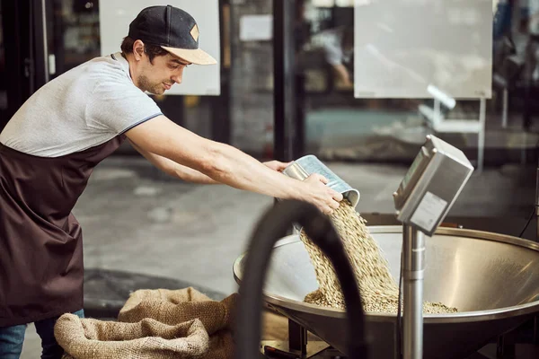 Joven guapo que pesa granos de café en la fábrica — Foto de Stock