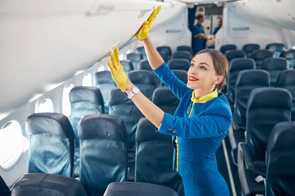 Hermosa azafata preparando y registrando compartimento con equipaje de mano en la cabina de pasajeros — Foto de Stock