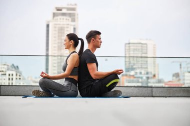 Genç çift şehir çatısında meditasyon yapıyor.
