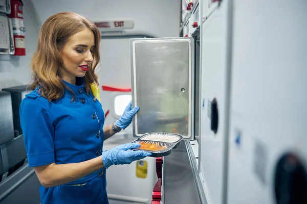 Sonriente azafata alegre pelo rojo preparando comida para los pasajeros de primera clase y de negocios — Foto de Stock