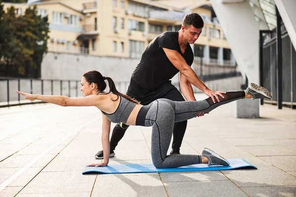 Male trainer assisting slim woman during workout outdoors — Stock Photo, Image