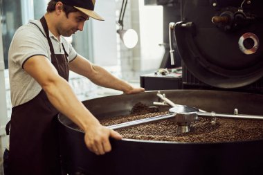 Profesyonel kahve kızartma makinesi kullanan yakışıklı erkek işçi.