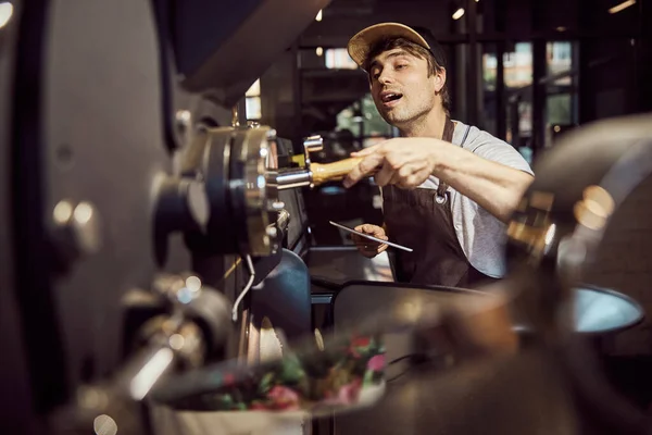 Hermoso trabajador masculino que controla el trabajo de la máquina de tostado de café — Foto de Stock