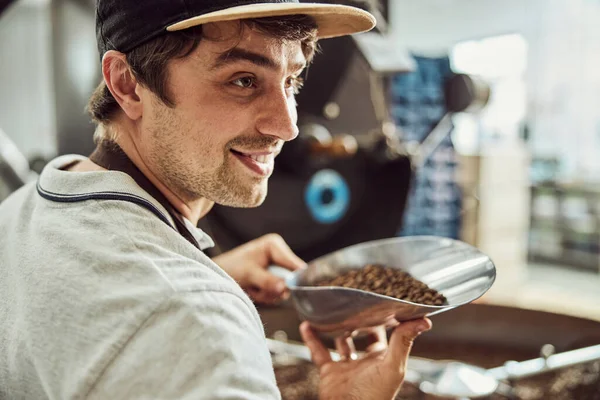 Guapo joven sosteniendo cucharada con granos de café — Foto de Stock