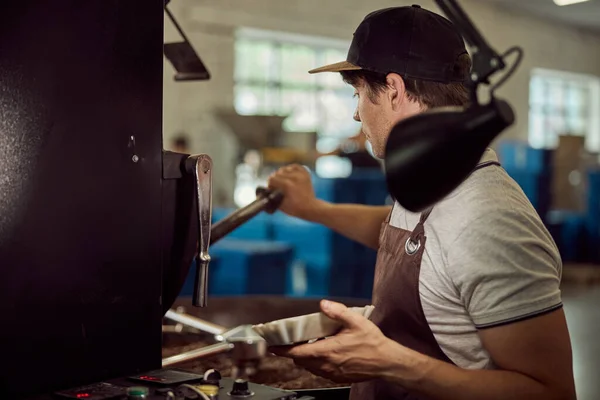 Άνδρας εργαζόμενος που χρησιμοποιεί βιομηχανική μηχανή ψησίματος καφέ — Φωτογραφία Αρχείου