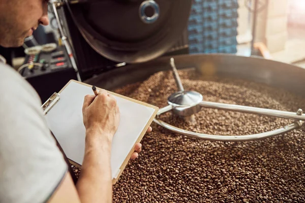 Male worker taking notes while using coffee roasting machine — Stock Photo, Image