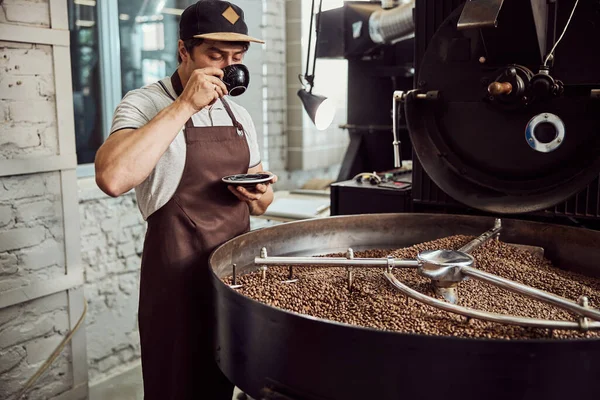 Trabajador masculino bebiendo café cerca de máquina de tostado de café —  Fotos de Stock