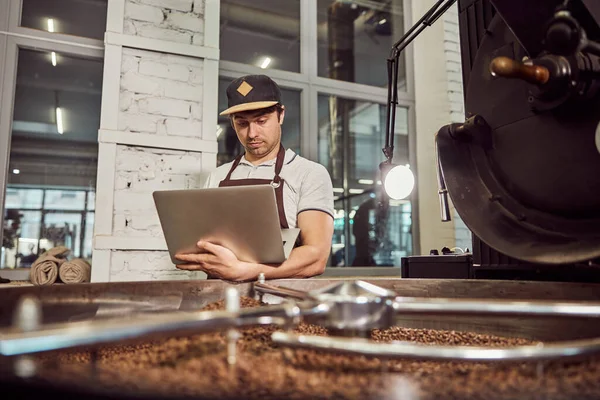 Guapo joven tostador profesional utilizando portátil en el trabajo — Foto de Stock