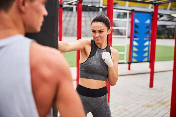 Cheerful young female hitting boxing bag outdoors — Stock Photo, Image