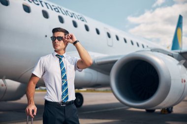 Havaalanında güneş gözlüğüne dokunan yakışıklı erkek pilot.
