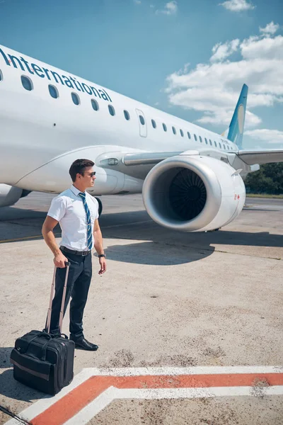 Piloto masculino bonito com mala de viagem em pé no aeródromo — Fotografia de Stock