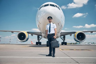 Neşeli erkek pilot havaalanında dikiliyor.