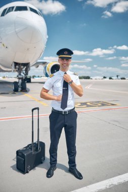 Yakışıklı erkek pilot havaalanında kravatını düzeltiyor.