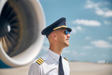 Güneş gözlüklü neşeli pilot dışarıda, havaalanında duruyor.
