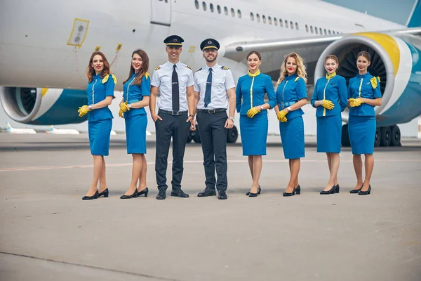 Handsome pilots and beautiful stewardesses standing outdoors in airfield — Stock Photo, Image