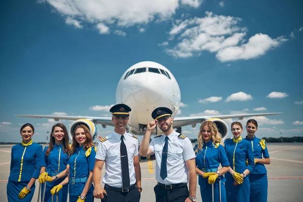 Cheerful airline workers standing in airfield under blue sky — Stock Photo, Image