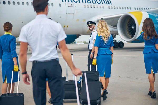 Aeromoças e pilotos que transportam sacos de bagagem de carrinho no aeroporto — Fotografia de Stock