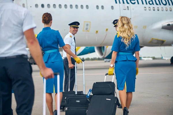 Pilotos y azafatas que transportan bolsas de viaje en el aeropuerto — Foto de Stock