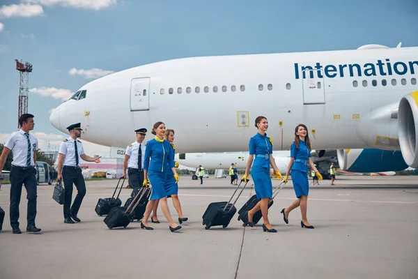Пилоты и стюардессы с дорожными сумками в аэропорту — стоковое фото