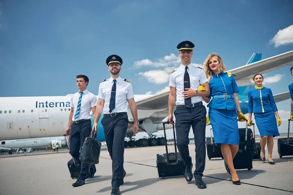 Vrolijke piloten en stewardessen met reistassen op de luchthaven — Stockfoto