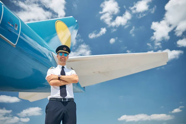 Cheerful pilot standing by airplane under blue sky — Stock Photo, Image
