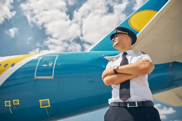 Guapo piloto masculino de pie junto al avión bajo el cielo azul — Foto de Stock