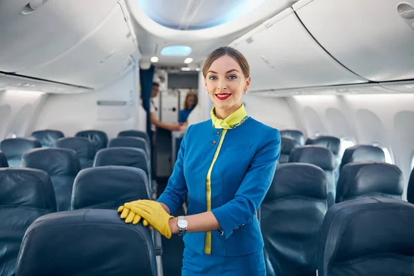 Młoda piękna stewardessa stojąca w alejce salonu pasażerskiego samolotu — Zdjęcie stockowe