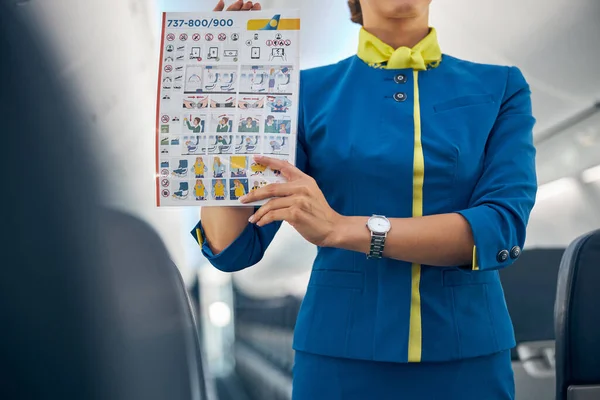 Jeune hôtesse de l'air attrayante tenant des instructions de sécurité sur un vol commercial dans les mains — Photo