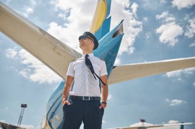Güneş gözlüklü neşeli erkek pilot güzel gökyüzünün altında duruyor.