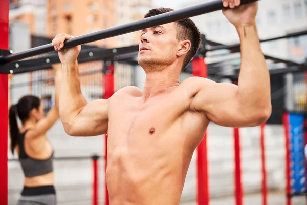 Homem muscular fazendo pull ups em campo de esportes — Fotografia de Stock